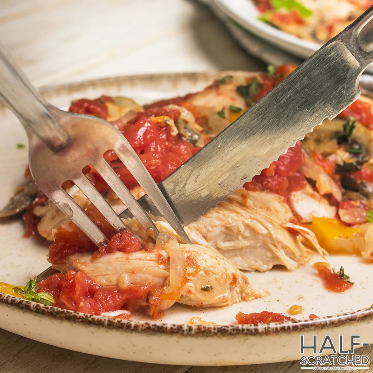 Chicken cacciatore being cut with fork and knife