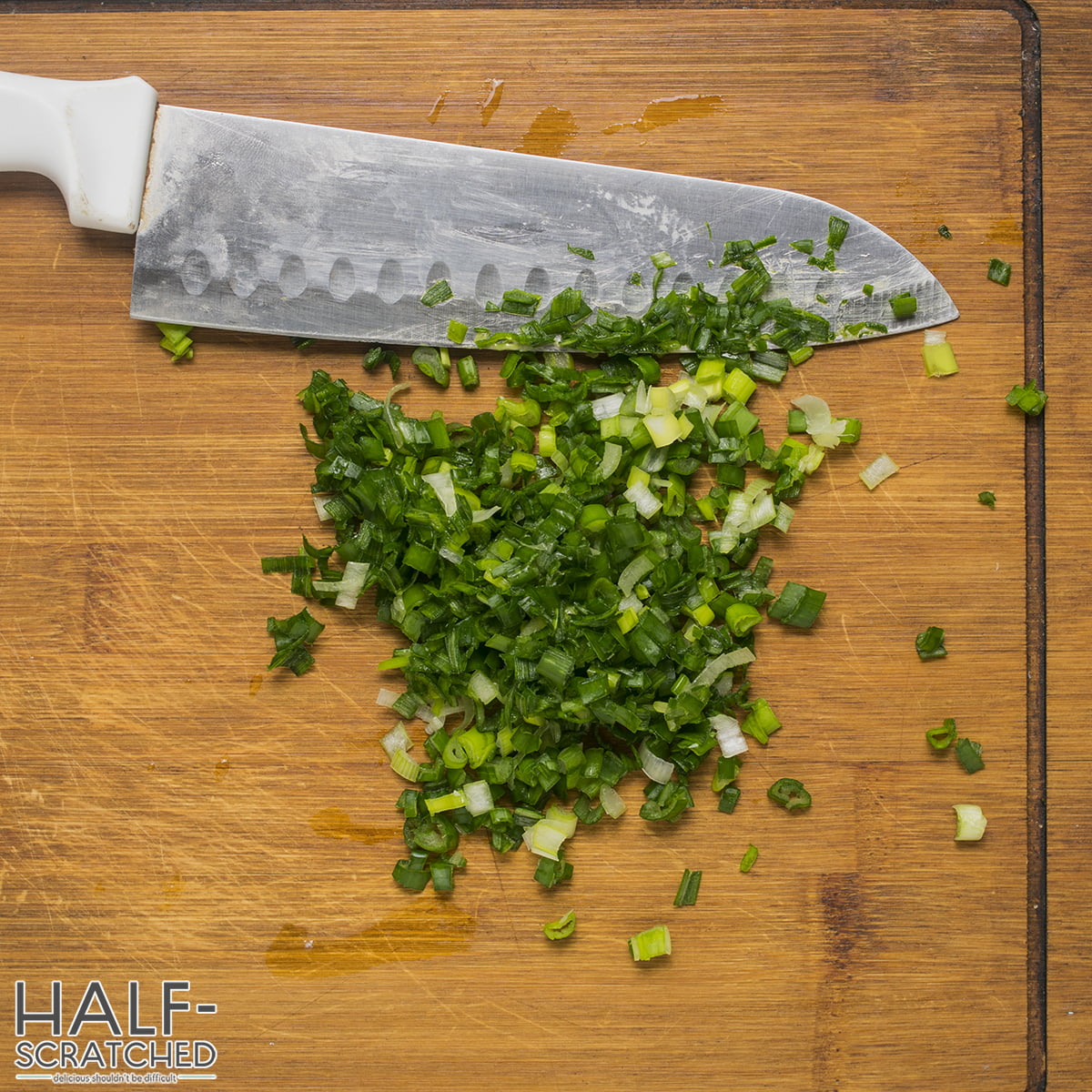 Chopped green onions on a wooden cutting board with a knife