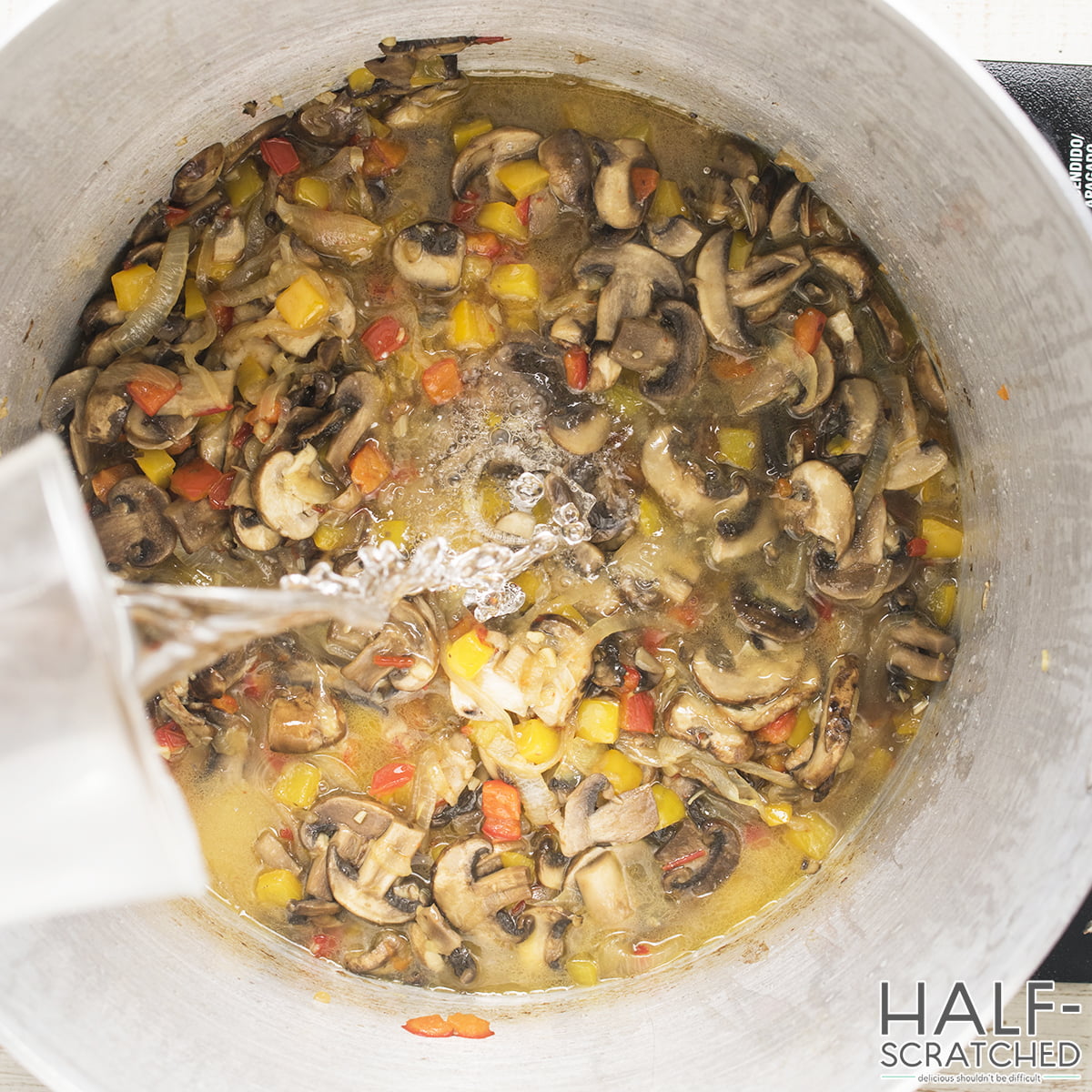 Vinegar being poured into a pot with mushrooms and bell peppers