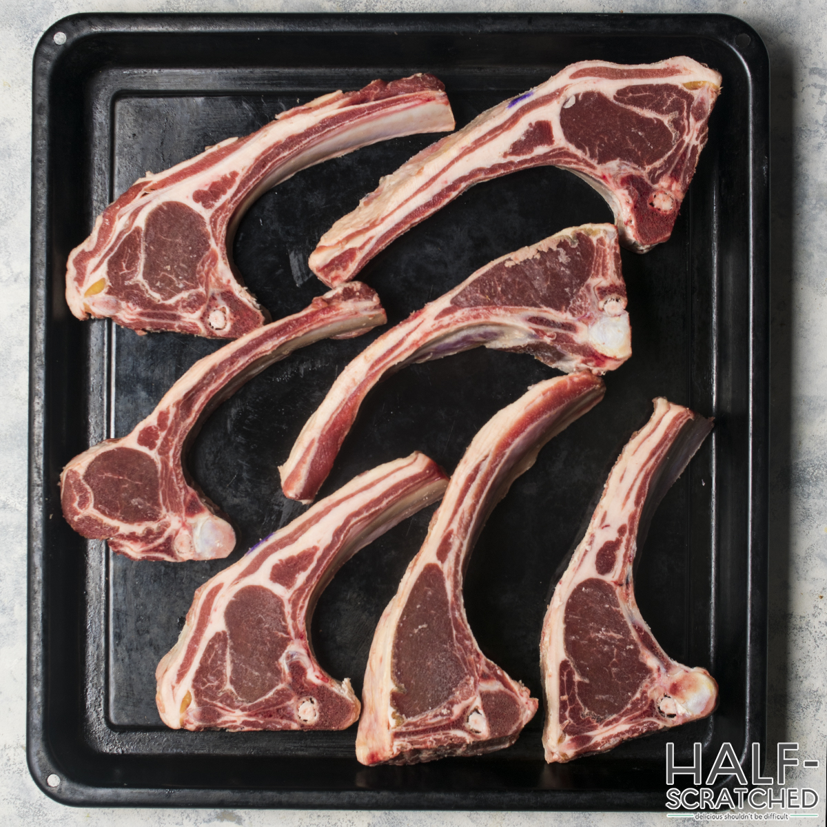 Raw lamb chops arranged on a black tray